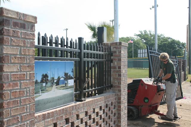 Hardscape installation — brick pillar and iron gate construction at athletic facility